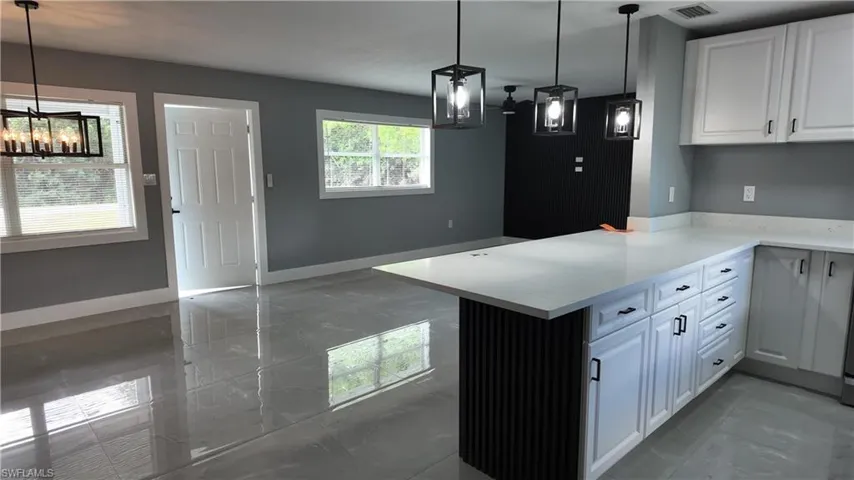 Kitchen featuring white cabinets, a peninsula, light marble finish flooring, and suspended lighting