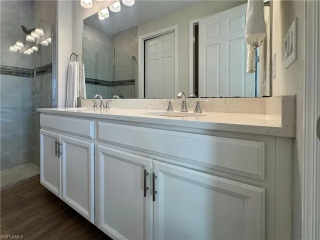 Full bath with double vanity, a stall shower, and dark wood-type flooring