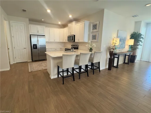 Kitchen featuring appliances with stainless steel finishes, white cabinets, a breakfast bar, decorative backsplash, and recessed lighting