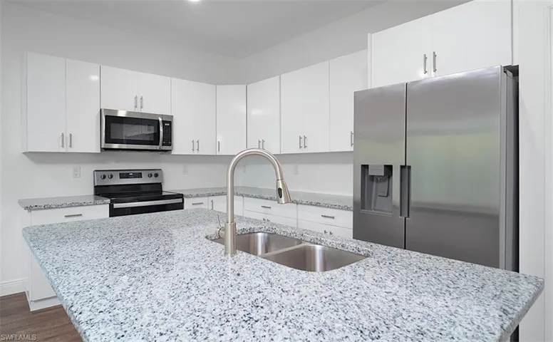 Kitchen featuring stainless steel appliances, white cabinetry, light stone countertops, and a center island with sink
