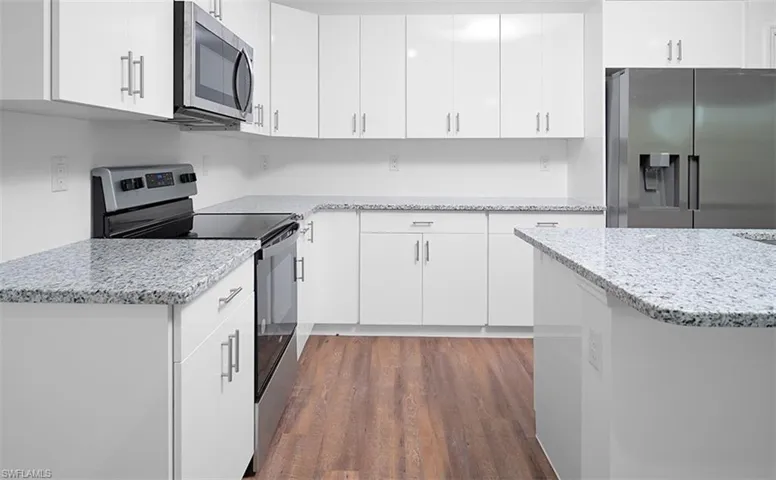 Kitchen featuring stainless steel appliances, light stone counters, white cabinetry, and dark wood finished floors