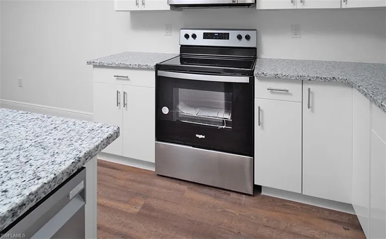 Kitchen featuring stainless steel appliances, white cabinets, light stone countertops, and dark wood-style floors