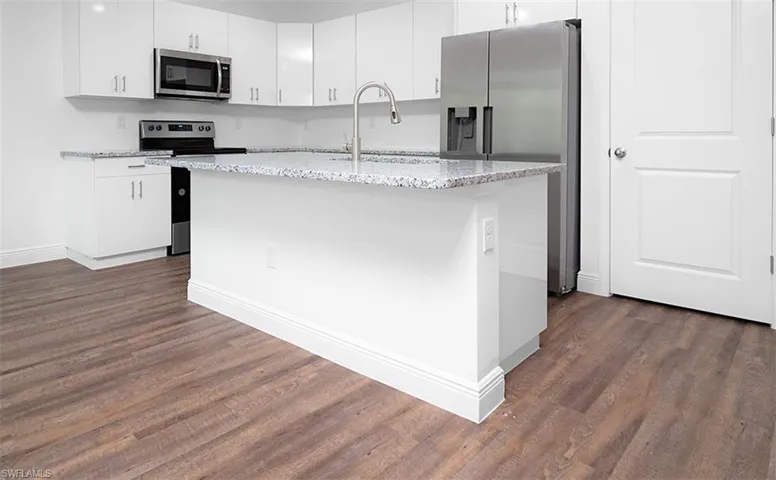Kitchen featuring appliances with stainless steel finishes, an island with sink, light stone counters, white cabinets, and dark wood finished floors