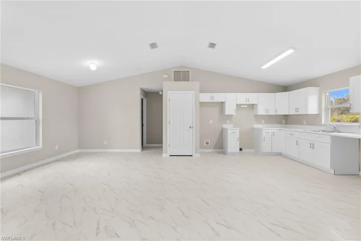 Kitchen with light countertops, white cabinetry, vaulted ceiling, and light marble finish flooring