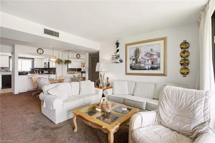 Open-concept living area featuring wall-to-wall carpeting and a kitchen with white cabinetry, black appliances, and a tiled backsplash