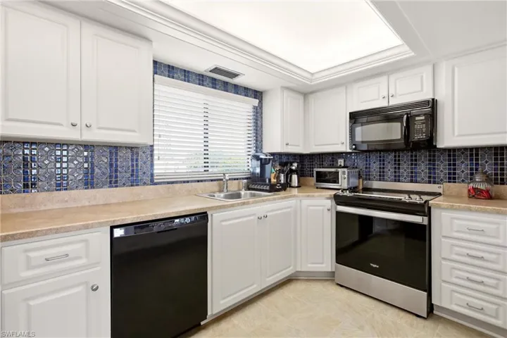 Kitchen featuring white cabinetry, blue mosaic tile backsplash, light-toned countertops, and stainless steel sink