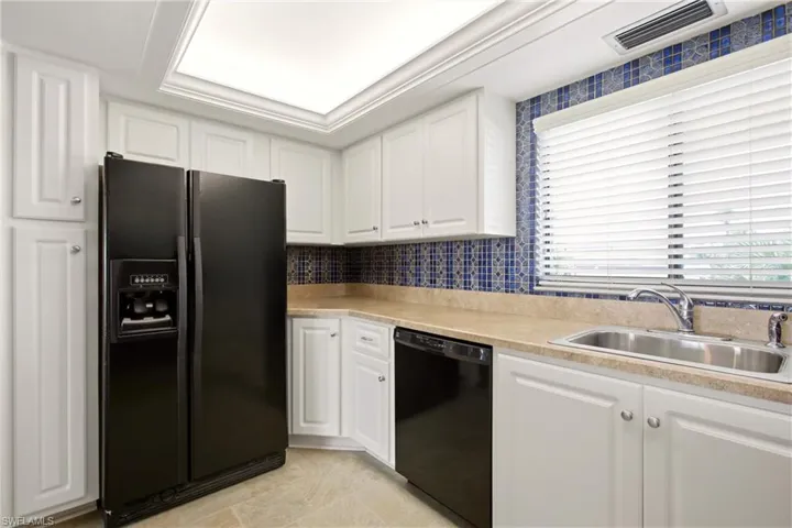 Kitchen featuring white shaker cabinetry, patterned blue tile backsplash, light-toned countertops, and a black side-by-side refrigerator