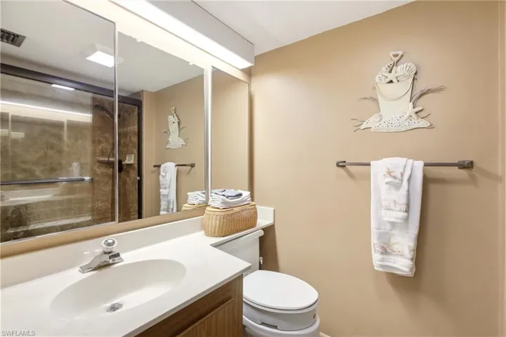 Bathroom featuring a vanity with an integrated sink, a large mirrored medicine cabinet, and a glass-enclosed shower with a tiled surround