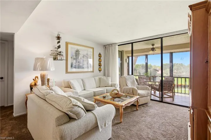 Living area with broad sliding glass doors opening to a screened balcony, featuring a ceiling fan and tiled flooring