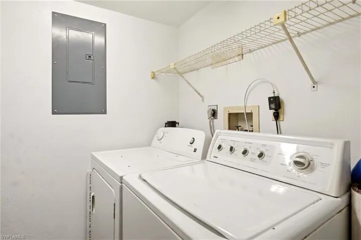 Dedicated laundry area featuring a white top-load washing machine and dryer, a wall-mounted wire shelving unit, and an electrical panel