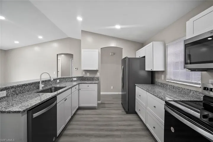 Kitchen featuring lofted ceiling, white cabinets, sink, wood-type flooring, and stainless steel appliances