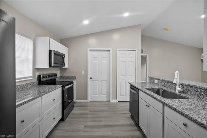 Kitchen with sink, vaulted ceiling, light hardwood / wood-style floors, white cabinetry, and stainless steel appliances