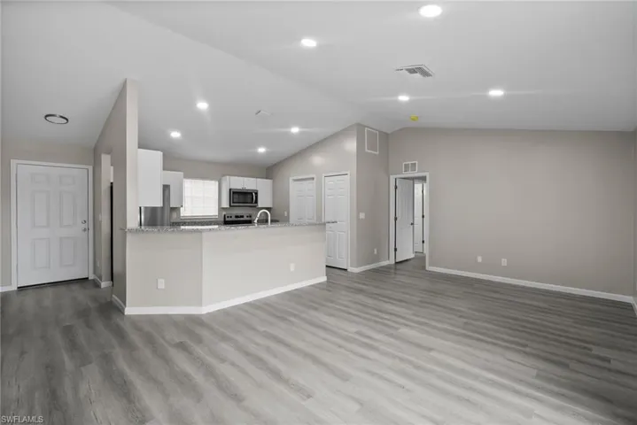 Kitchen with kitchen peninsula, appliances with stainless steel finishes, vaulted ceiling, light hardwood / wood-style floors, and white cabinetry