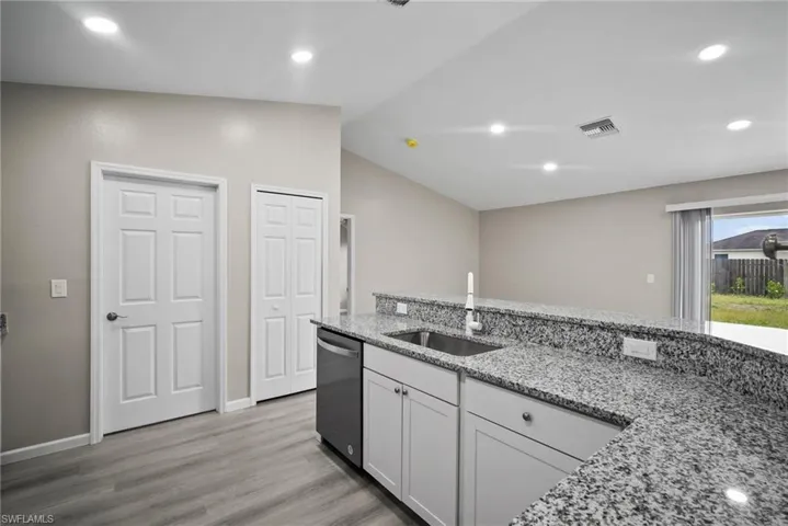 Kitchen featuring dishwasher, sink, light stone counters, lofted ceiling, and white cabinets