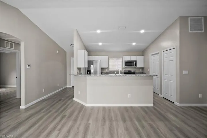 Kitchen featuring stainless steel appliances, light stone counters, light hardwood / wood-style floors, lofted ceiling, and white cabinets