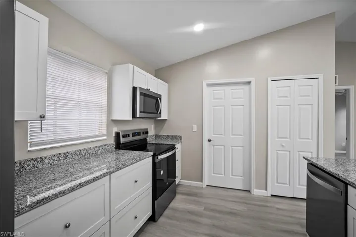 Kitchen with light stone counters, stainless steel appliances, light hardwood / wood-style flooring, white cabinetry, and lofted ceiling