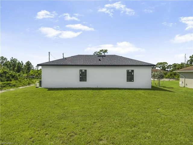 Back of property featuring a yard, stucco siding, and a shingled roof