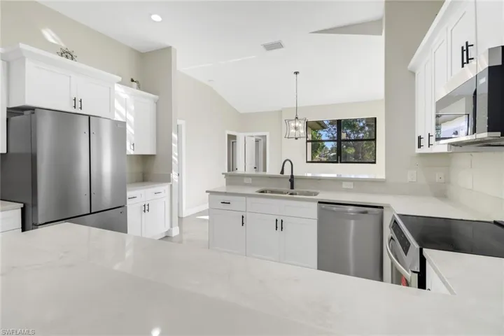 Kitchen featuring sink, white cabinets, stainless steel appliances, and decorative light fixtures