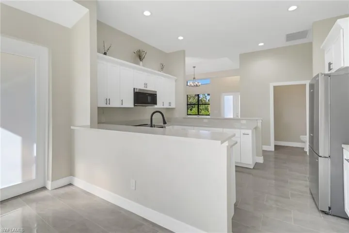 Kitchen featuring pendant lighting, an inviting chandelier, white cabinets, appliances with stainless steel finishes, and kitchen peninsula