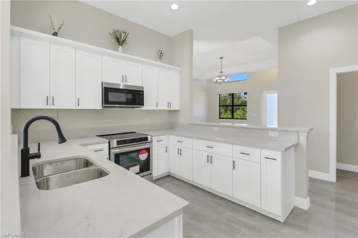 Kitchen with pendant lighting, white cabinets, sink, kitchen peninsula, and stainless steel appliances