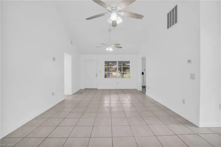 Empty room with light tile patterned flooring, high vaulted ceiling, and ceiling fan