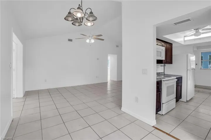 Kitchen featuring ceiling fan with notable chandelier, lofted ceiling, white appliances, and light tile patterned floors