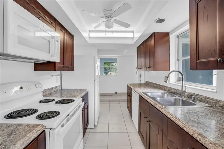 Kitchen featuring ceiling fan, a tray ceiling, white appliances, sink, and light tile patterned floors