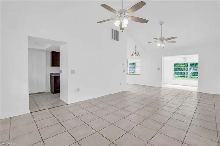 Empty room with ceiling fan with notable chandelier, light tile patterned floors, and high vaulted ceiling