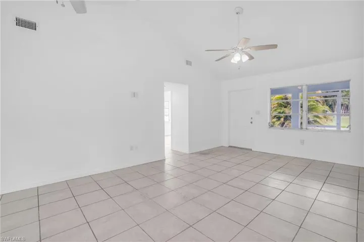 Tiled empty room with ceiling fan and high vaulted ceiling
