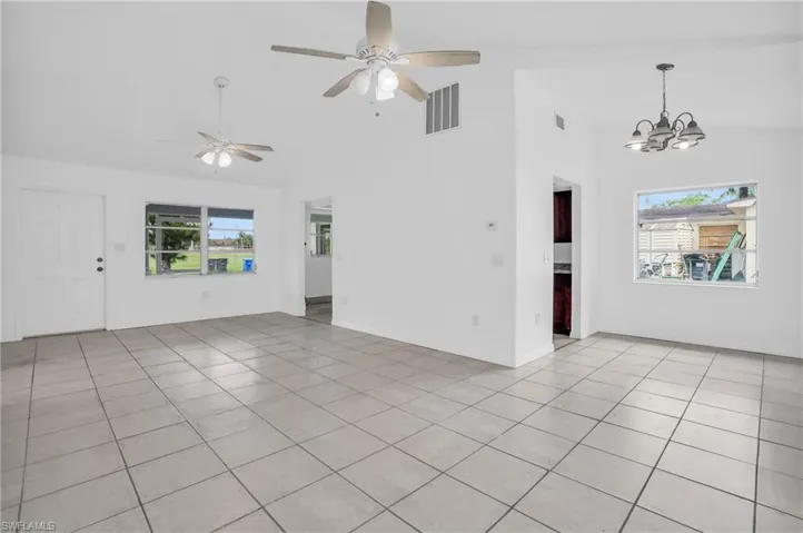 Spare room with high vaulted ceiling, ceiling fan with notable chandelier, a wealth of natural light, and light tile patterned floors