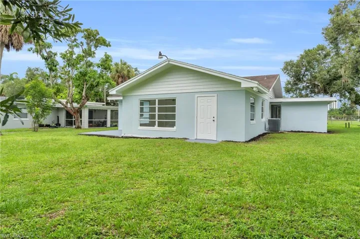 Rear view of property with central air condition unit and a lawn
