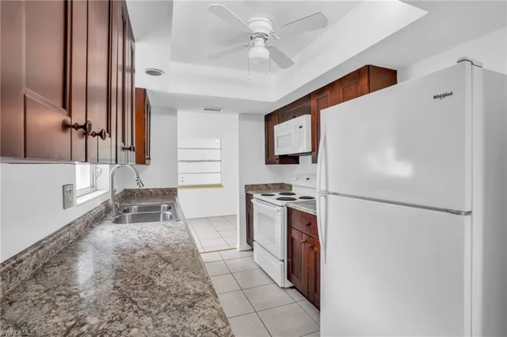 Kitchen with ceiling fan, white appliances, sink, a raised ceiling, and light tile patterned floors