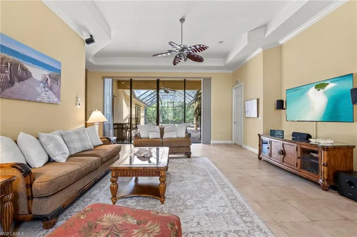 Living room featuring a tray ceiling, crown molding, light tile patterned floors, ceiling fan, and baseboards