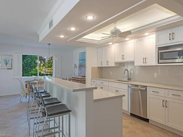 Kitchen featuring white cabinetry, solid-surface countertops, stainless steel appliances, recessed ceiling lighting, and a breakfast bar