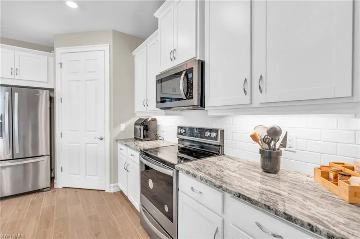 Kitchen with backsplash, white cabinetry, light hardwood / wood-style floors, stainless steel appliances, and light stone counters