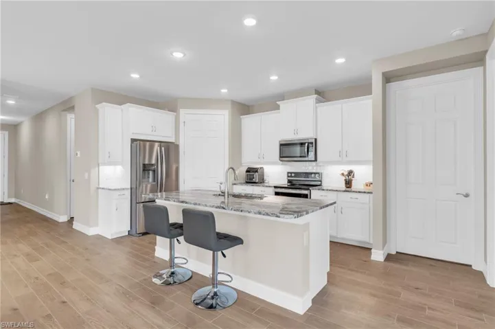 Kitchen with a kitchen island with sink, light stone countertops, light wood-type flooring, white cabinetry, and appliances with stainless steel finishes