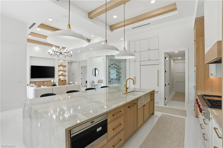 Kitchen featuring light stone countertops, a large island with sink, built in appliances, pendant lighting, and modern cabinets