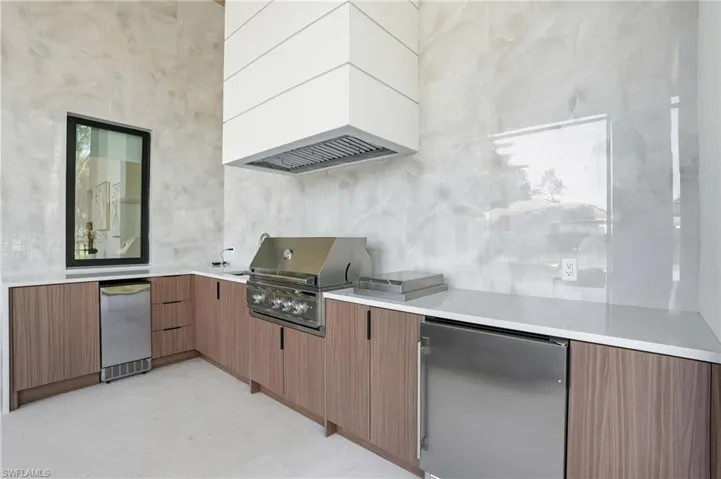 Kitchen with modern cabinets, stainless steel fridge, light stone countertops, brown cabinets, and light floors