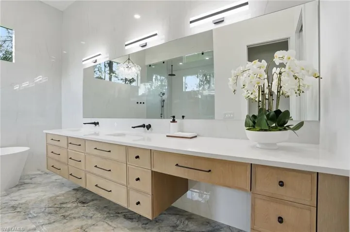 Full bathroom with double vanity, a shower stall, light marble finish flooring, and a freestanding bath