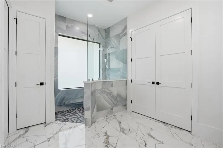 Full bath featuring light marble finish flooring and a marble finish shower