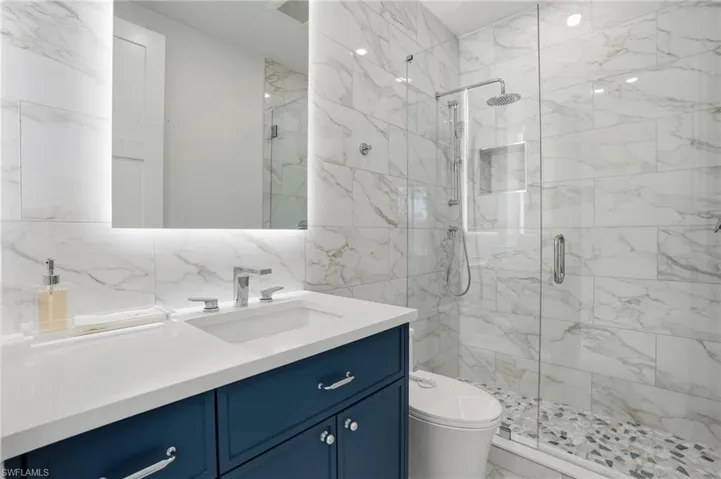 Bathroom with tile walls, vanity, a marble finish shower, and light marble finish floors