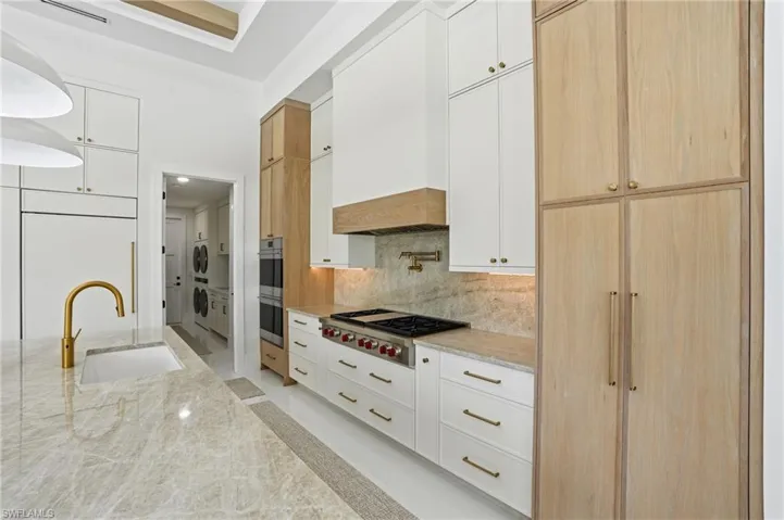 Kitchen featuring white cabinets, light brown cabinetry, light stone countertops, and backsplash