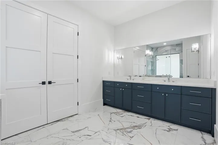 Bathroom featuring light marble finish flooring, a marble finish shower, and double vanity