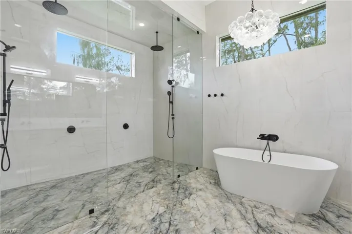 Bathroom featuring marble tiled flooring, a marble finish shower, a freestanding bath, tile walls, and a chandelier