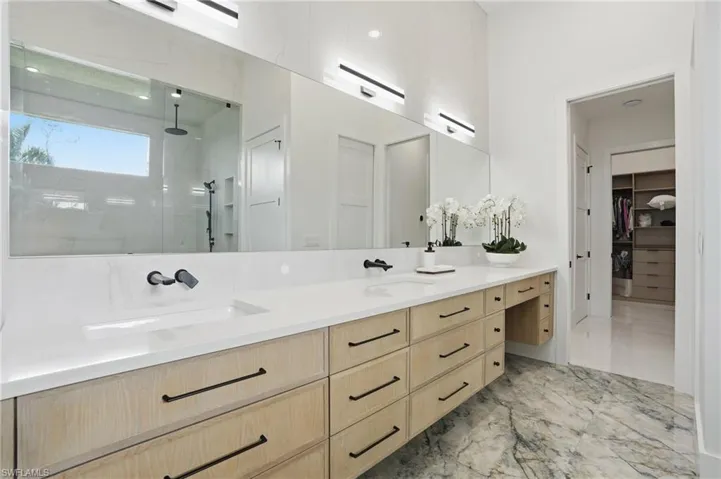 Bathroom featuring a stall shower, double vanity, a spacious closet, and light marble finish flooring
