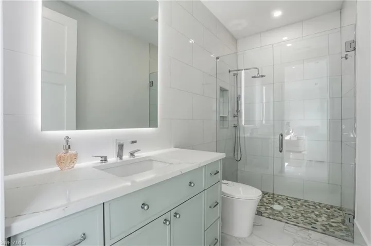 Bathroom with vanity, a stall shower, light marble finish flooring, and tile walls