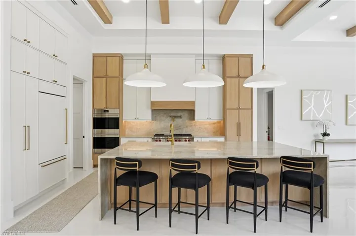 Kitchen featuring light stone counters, pendant lighting, white cabinetry, backsplash, and a spacious island