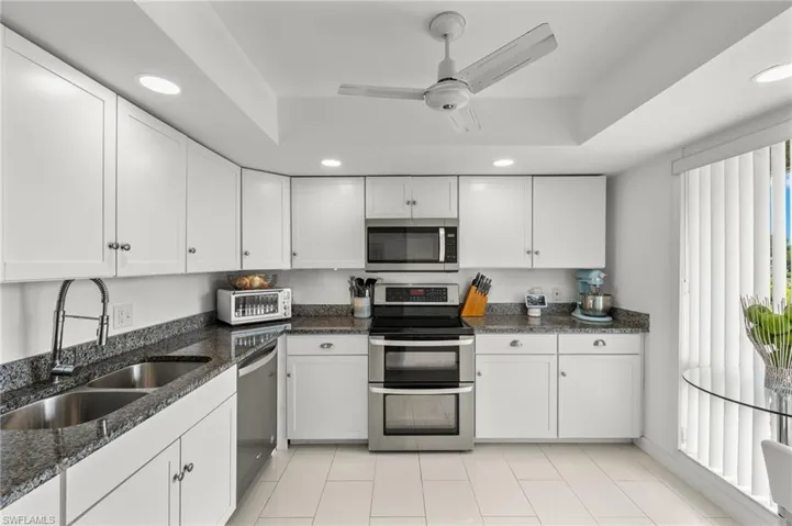 Kitchen with appliances with stainless steel finishes, sink, light tile patterned floors, white cabinetry, and ceiling fan