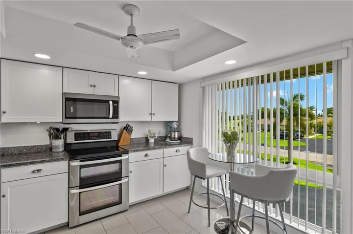 Kitchen dark stone countertops, white cabinets, ceiling fan, and appliances with stainless steel finishes