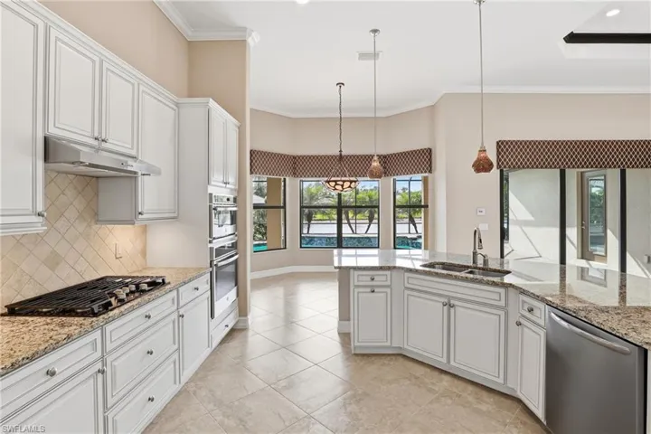 Kitchen with white cabinetry, stainless steel appliances, pendant lighting, light stone counters, and ornamental molding